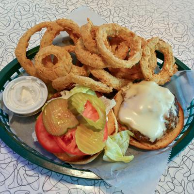 Cheeseburger with lettuce, tomato, pickles, side of onion rings and a dip.