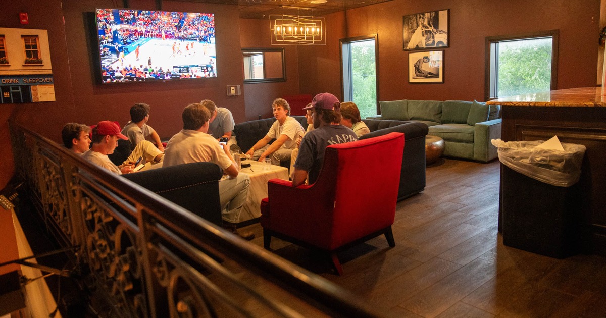 Lounge area with people sitting around a table watching a basketball game on TV