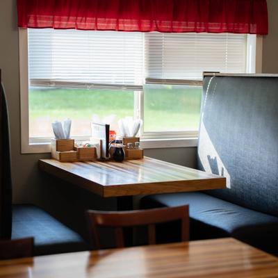 Cozy booth setup with a small wooden table and dark upholstered seating by a window.