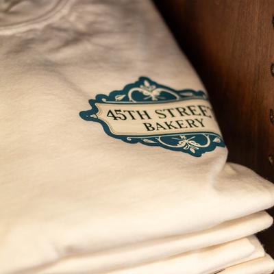 Folded white t-shirts featuring the 45th street bakery emblem.