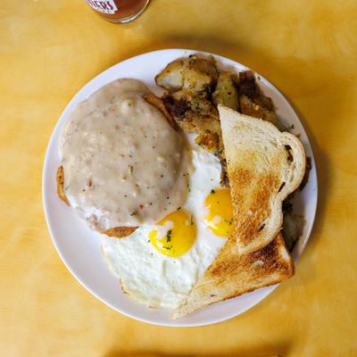 Country Fried Steak with gravy, breakfast potatoes, sunny side up eggs, and toast.