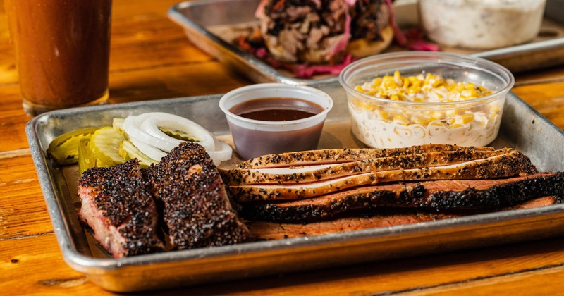 Smoked brisket served on a tray with creamed corn and BBQ sauce