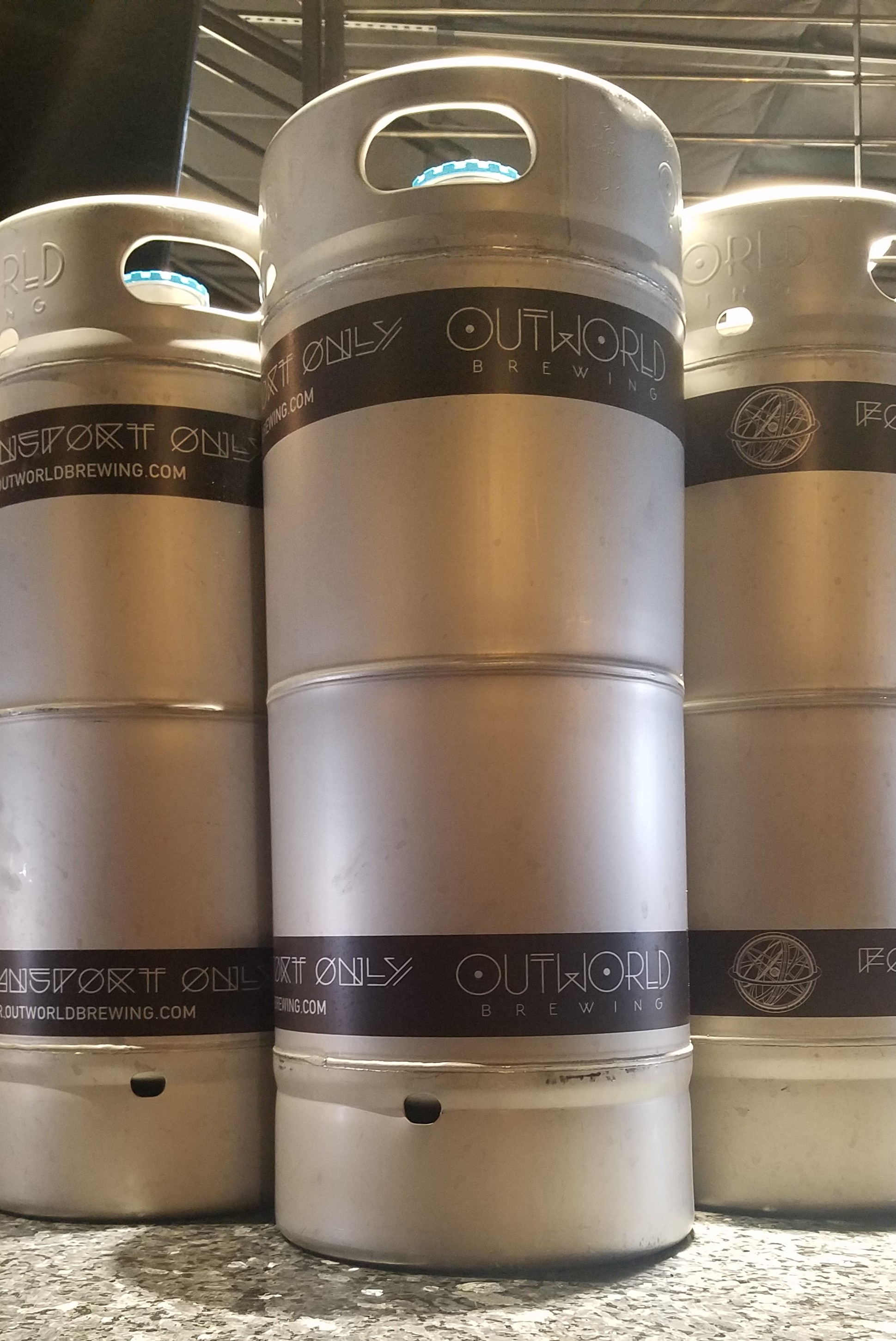 Upward shot of three silver sixtel kegs with a purple band that says 