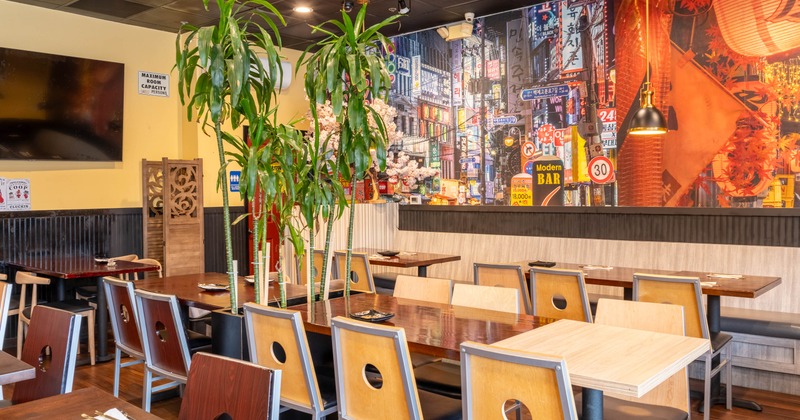 Interior of a modern restaurant with tables, chairs, and a cityscape mural on the wall