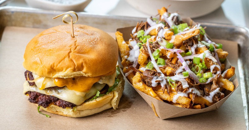 A cheeseburger next to loaded fries topped with green onions