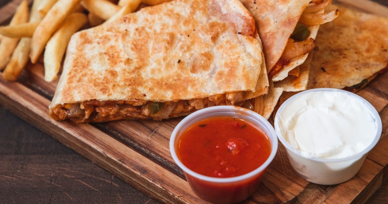 Quesadillas, fries and dipping sauces on a wooden board