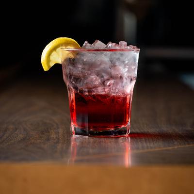 A glass of home made strawberry vodka sits on a bar counter.