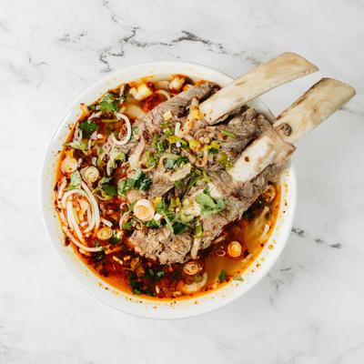 Spicy beef pho bowl rests on a white marble surface.