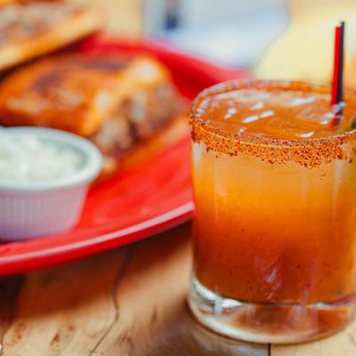 Chili-rimmed cocktail in a rocks glass with a plated dish in the background.
