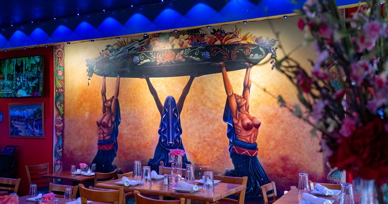 Dining area with set tables by the wall with a large, colorful mural