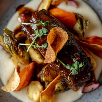Braised short rib with root vegetables, microgreens, and crispy chips on mashed potatoes.