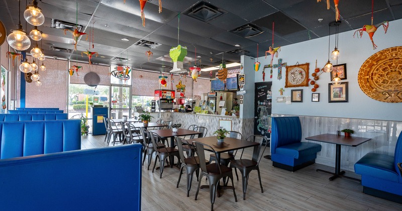 Mexican-style interior - blue booths, dining tables, hanging decorations, pendant lights.