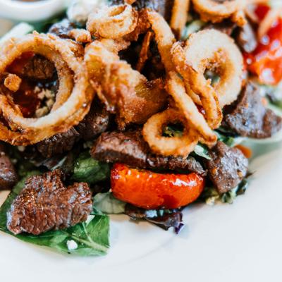 Grilled steak salad topped with onion rings.