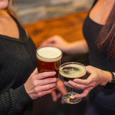 Two patrons share a toast, holding a pint of beer and a cocktail.