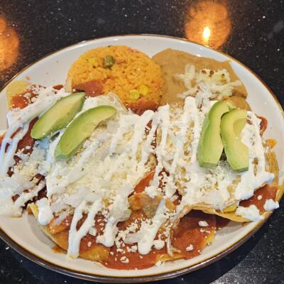 Chilaquiles topped with avocado, crema and cheese, served with rice and beans.