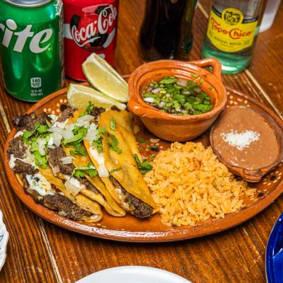 Quesabirria tacos served with rice , beans lime wedges and consomme.
