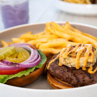 An open-faced burger with fries, fresh toppings, and a small crab cake.