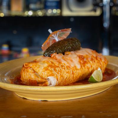 Burrito covered in sauce, garnished with a lime wedge, grilled jalapeno and a umbrella.