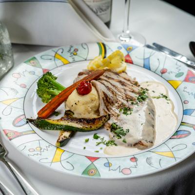 A plate of grilled fish and vegetables on a colorful, patterned rimmed plate.