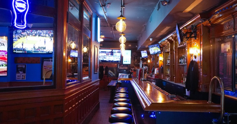 Interior of a bar with a long wooden counter, bar stools, multiple TVs, wood coated walls