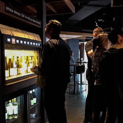 A dimly lit wine bar with people selecting bottles from a glowing wine dispense.