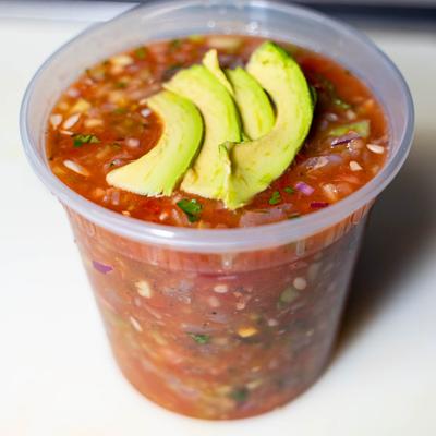 Ceviche served in a plastic cup and topped with avocado slices.