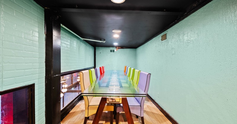 A narrow room with a long glass table and colorful high-backed chairs