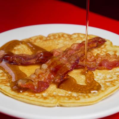 Pancakes topped with bacon, being drizlled with syrup.