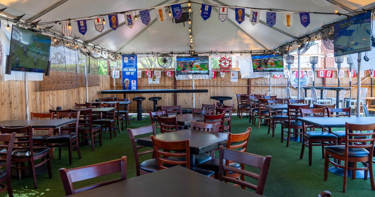 An outdoor tented dining area with wooden tables and chairs