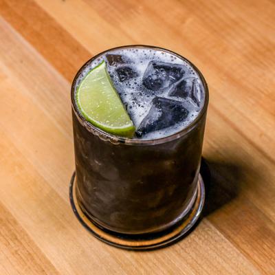 Dark cocktail on the rocks with a lime wedge.