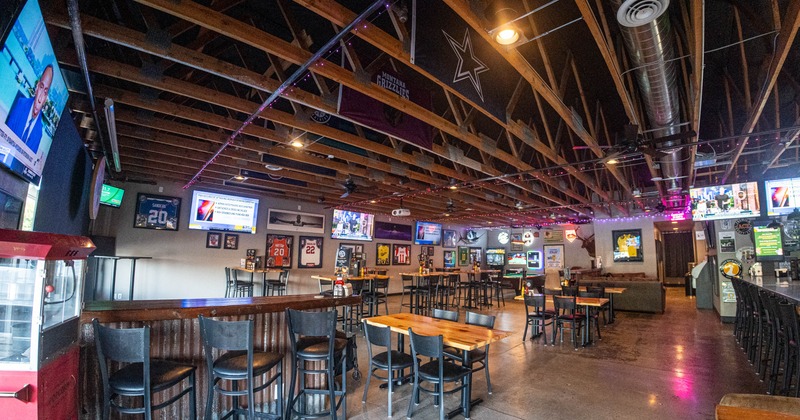 Interior of a sports bar with high top tables, black chairs, multiple TVs on the walls