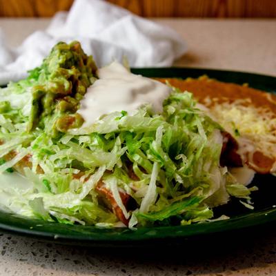 Chimichangas, covered in cheese and red sauces, lettuce, sour cream, guacamole, and a side of beans.