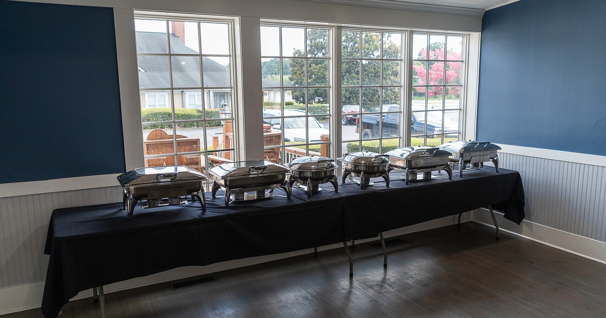 Buffet setup with chafing dishes arranged on a long table with a black tablecloth