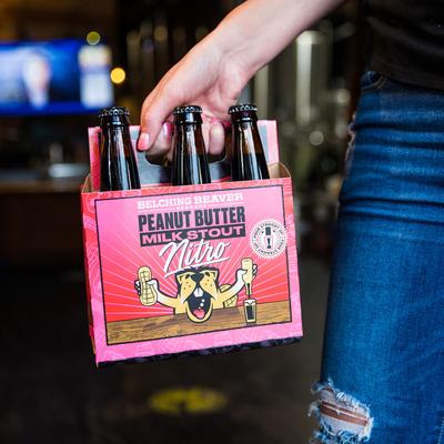 A person holding a box with bottles  of Belching Beaver Peanut Butter Milk Stout Nitro.