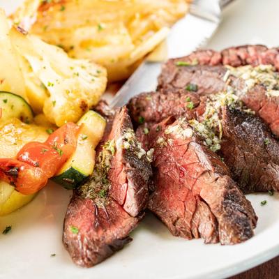 Sliced hanger steak with herbed butter, au gratin potatoes, and vegetables.