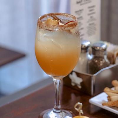 Cocktail in a wine glass garnished with dry apple and cinamon stick.