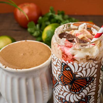 Chocolate dessert drink with whipped cream and candy next to hot cocoa in a white mug.