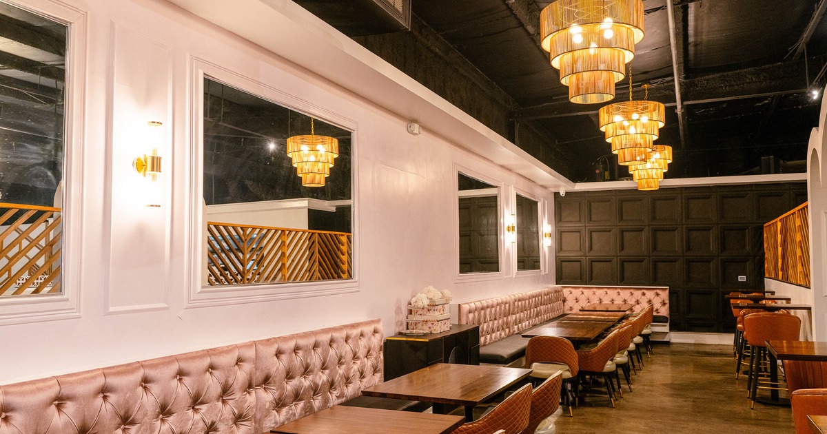 An elegant interior - mirrors, pink tufted seating, dark wood tables, tiered gold chandeliers