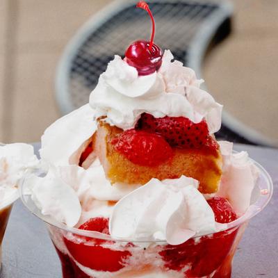 Strawberry shortcake in a clear cup topped with whipped cream and a cherry.