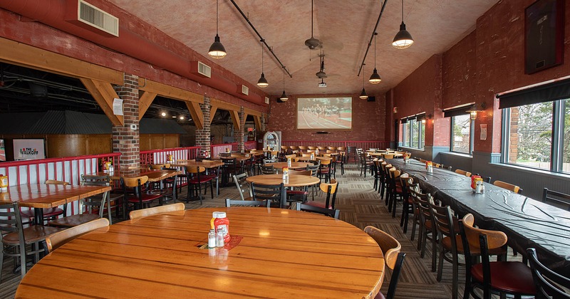 Interior, lined up tables and chairs by the wall, tv screens on the wall