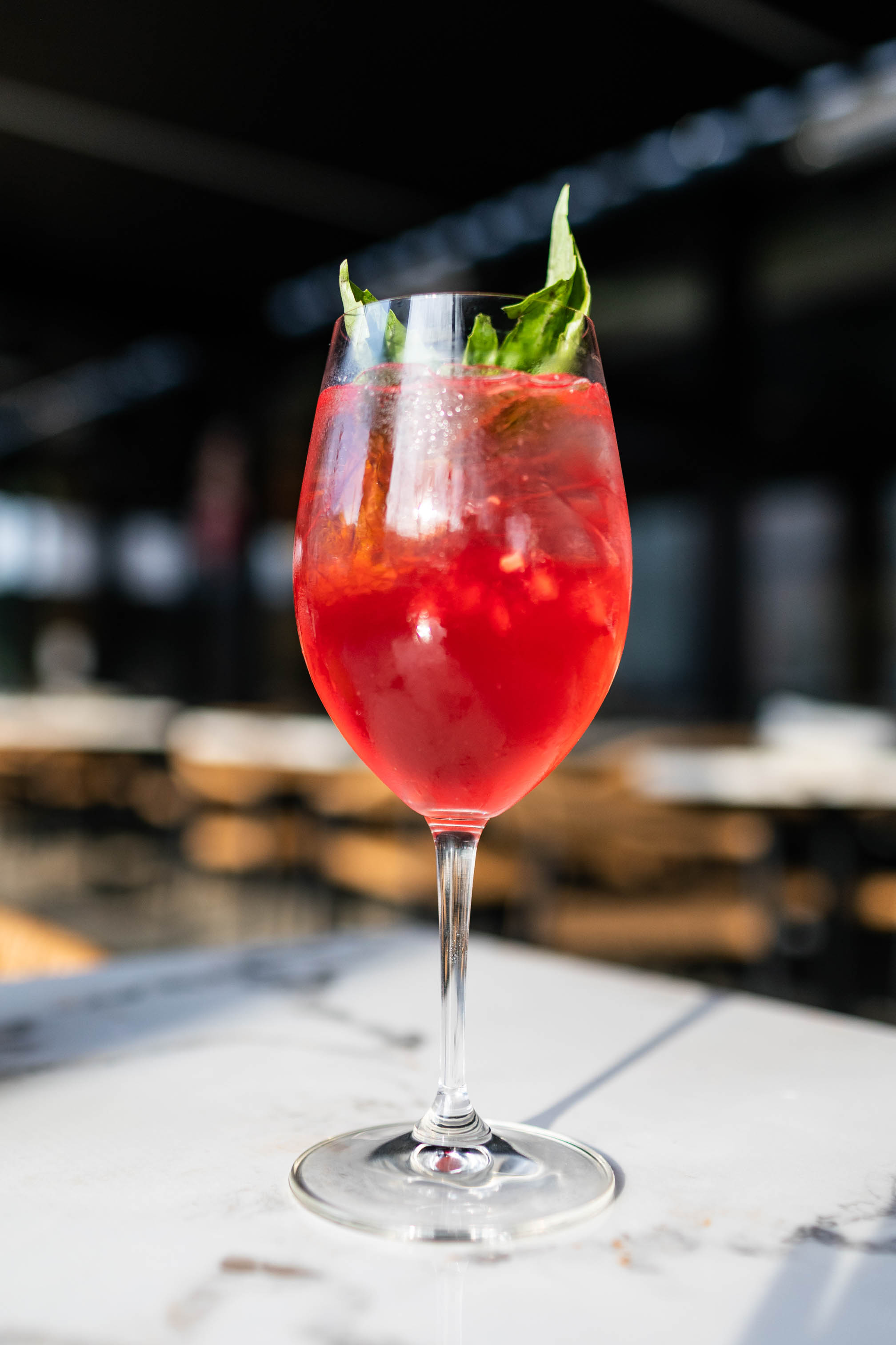 red cocktail in a wine glass with sprig of fresh herb garnish