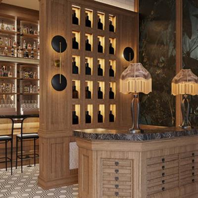 Bar area with wooden cabinetry with inset shelving for bottles and table lamps.