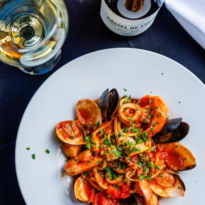 Seafood pasta with clams, mussels, shrimp, and tomato sauce served beside white wine.