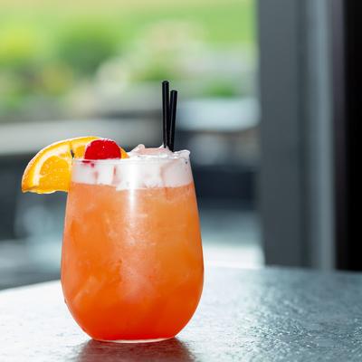 Sex on the Beach cocktail glass garnished with a cherry, black straws, and an orange slice.