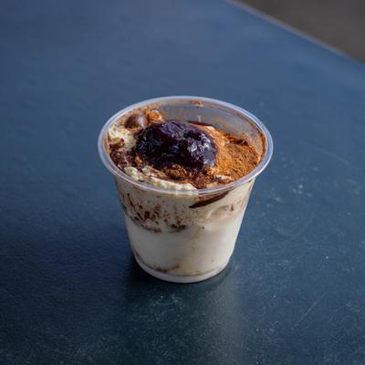 Tres Leches Tiramisu served in a plastic cup on a dark table.
