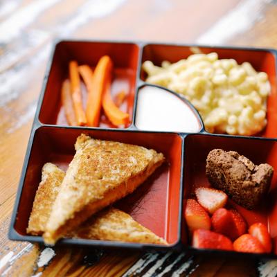 Kids bento box with grilled sandwich, carrot sticks, mac and cheese, and strawberries.