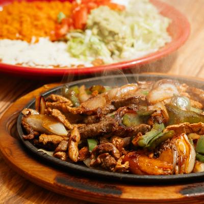 Steaming hot beef and chicken fajitas with peppers and onions.
