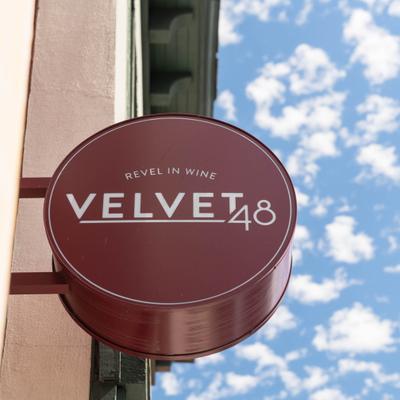 Round Velvet 48 wine bar sign against a blue sky with clouds.