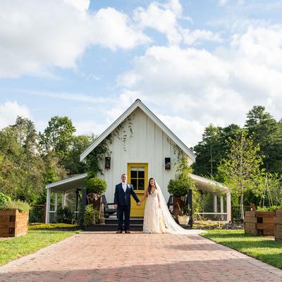 Wedding couple stand hand in hand on a brick path in front of a charming white cottage