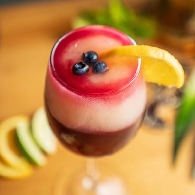 Layered berry cocktail garnished with blueberries and orange.